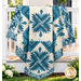 The completed Cactus in the Cabin quilt, colored in cream and blue fabrics from the Special Delivery collection by Andover Fabrics, artfully draped over a white porch railing beside coordinating florals.