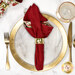 A top down shot of the napkin with the red fabric facing out, staged on a coordinating gold table setting on a white marbled table.