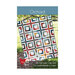 The front of the Orchard pattern featuring a multicolor floral and plaid quilt with a geometric hollow square grid pattern hung on a tree branch in a natural setting.