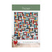The front of the Thicket pattern featuring a multicolor quilt with a rotating strip piece block pattern hung on a white wall.