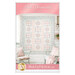 The front cover of the Pink Diamonds pattern showing the completed quilt colored in pastel pink, blue, and cream fabrics, staged on a white wall with coordinating furniture and décor.