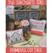 Cross-stitch sampler display with sewing supplies and “Primrose Cottage” title.