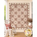 The completed Morning Blush quilt, colored in gentle red, cream, brown, and pastel pink fabrics from the Yardley House collection from Marcus Fabrics, staged on peachy cream porch wall with coordinating furniture and décor.