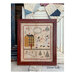Finished Snow Folly pattern of snowmen dancing around a manor and train tracks in a distressed red frame in front of a quilt and wooden backdrop.