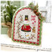 A fully assembled and painted Scalloped Arbor Frame Cross Stitch Display, staged on a white tabletop with coordinating decor, displaying a completed Holly Jolly cross stitch project.