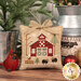 A close up on a completed ornament, featuring a red barn with green doors, surrounded by two sheep and a cardinal.