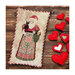 Finished Special Delivery cross stitch pattern of Santa in an apron holding kittens stitched on a pillow placed on a wooden plank backdrop sided by hearts.