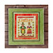 Finished Gather cross stitch pattern with two pilgrims holding Thanksgiving food in a green frame laid on wooden planks.