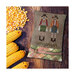 Finished Autumn Scarecrows pattern on a small decorative pillow next to a pile of corn kernels and corn on the cob.