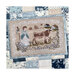 Finished Bessie in the Bluebells pattern of a shepherd herding cows in front of cottages surrounded by an ornamental white accent laying on a blue and white quilt.
