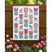 The Birds and Blooms quilt, colored in bright fabrics from the Floriori collection by Moda Fabrics and staged on a wooden fence in a garden of tulips.
