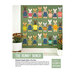 Front cover of the finished The Bunny Bunch sampler quilt with bunnies on a green fabric hung on a white wall with sunflowers on both sides of it.