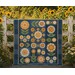 The completed Fresh As A Daisy Quilt, draped over a wooden fence surrounded by a garden of sunflowers.