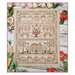 Finished April Sampler cross stitch pattern on a beige fabric surrounded by berries, florals, and carrots.
