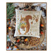 Finished The Little Squirrel cross stitch pattern on a decorative linen colored pillowed on a wood stand surrounded by acorns and pinecones.