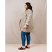 A model wearing the long coat of black accented leaves on a cream fabric, blue jeans, and sandals.