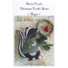 Front cover of the Animal Cracker Christmas Cookie Series Sugar pattern with the skunk doll fully finished on top of some old paper and quilting supplies.