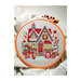 Christmas House cross stitch pattern with a red and tan house covered in snow and ornaments surrounded by presents set in a circular hoop.