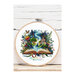 Finished Magic Book cross stitch pattern inside of a hoop display on white cloth in front of a wooden backdrop.