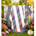 The completed 28th Floor Quilt colored in white blue, and a rainbow of fabrics from the Kipling Gardens collection by Riley Blake Designs, artfully draped over a white fence in a lush garden.