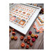 Dynamic angle of the finished Pumpkin Hollow cross stitch pattern inside of a white frame surrounded by small pumpkins, fabrics from Moda's Birch and Willow fabric line, and smaller accent pillows.