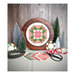The Whimsy Star cross stitch pattern showing the finished product in a wooden circle hoop next to frosty prop trees, a snowflake, the Moda Poinsettia and Pear line, and a tub of buttons.