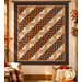 The completed Log Cabin Throw Quilt, colored in black, brown, tan, orange, and cream fabrics from the Midnight Cheddar collection from Marcus Fabrics, hung on a sunlit living room wall and staged with coordinating furniture.