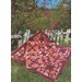 One of the quilts draped across grass and a fence in front of a flowering tree.