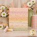 A stack of the fabrics included in the Dear Daisy collection, with flowers and vases and a mug and thread and the included panel.