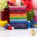 A stack of the fabrics included in the Paradise Batiks collection, with flowers and jars and thread and a ceramic bird.