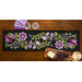 The completed Baltimore Garden Table Runner in violet, staged on a wooden table with four black chairs, two wine glasses, fabric, and a serving plate with cheese and grapes.