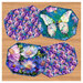 Four panel placemats in bright floral and butterfly themed fabrics on a wooden tabletop background.