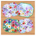 Four panel placemats in bright floral fabrics on a wooden tabletop background.