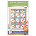 The front cover of the Mosaic Diamonds pattern showing the completed quilt colored in a rainbow of fabrics, staged on a white wall with coordinating furniture and décor.