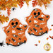 The two completed Ghostly Hot Pads, colored in orange and black fabrics from the Frank and Friends collection, staged on a white table with coordinating décor and candy corn.