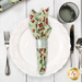 A top down shot of the napkin with the green fabric facing out, staged on a coordinating table setting on a white wooden table.