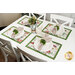 Lifestyle shot of a white dining table with the four Christmas-themed white and green placemats, coordinating plates, and folded napkins.