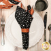 A top down shot of the napkin with the black and white star print side out, showcasing the geometric print; the napkin is staged with a cream plate and matching table setting.