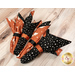 An angled shot of the four napkins colored in the Purrs and Boos collection from Moda Fabrics, featuring cute Halloween themed prints, staged on a wooden table.