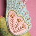Close-up of the felted pink and blue wing with stitched details on a pink background.