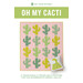 Front cover of the Oh My Cacti pattern featuring a pink quilt with cacti in various shades of green with a snake pillow in the corner.