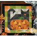 A top down shot of the first block of the Mystery BOM, a Fusible Grid patchwork block of a black cat with an orange pumpkin with yellow laser cut appliqué pieces, staged with coordinating leaves, spooky cobwebs, and candy corn. A gold banner with the Shabby Fabrics logo reads "Fusible Grid."
