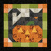 A top down isolated shot of the first block of the Mystery BOM, a Fusible Grid patchwork block of a black cat with an orange pumpkin with yellow laser cut appliqué pieces.