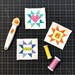 Quilt blocks on a cutting mat with rotary cutter and thread spools.