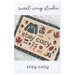 The front of the Stay Cozy cross stitch pattern, showing the completed project styled on a shag rug.