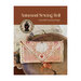Front cover of the Autumnal Sewing Roll cross stitch pattern displaying the finished design folded up and placed on a log next to a white doily.