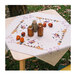 Close up lifestyle shot of the completed Halloween tablecloth staged on a small table outdoors among fallen leaves, staged with coordinating décor and lantern fruit. 