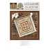 Front of pattern showing the completed cross stitch on a small ornament pillow staged on a table by autumnal sprigs.