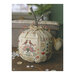 The finished Autumn Abundance pumpkin pincushion cross stitch pattern with a stick down the middle on a wooden table.