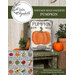 The finished pattern as a cushion displayed on a chair with plants and pumpkins..